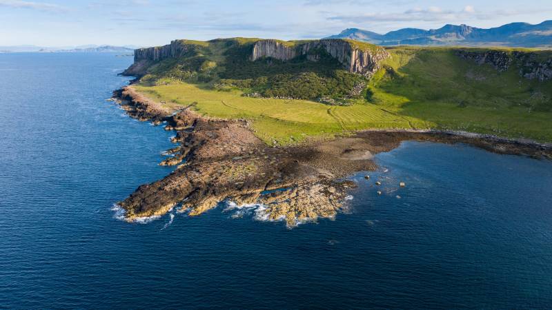 Dramatic cliffs rise from the deep blue sea, overlooking a rugged coastline and verdant green hills.