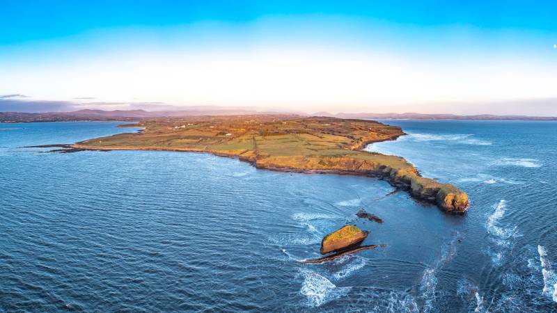 Golden hour illuminates a rugged Irish coastline with rolling green fields meeting the vast, blue ocean.