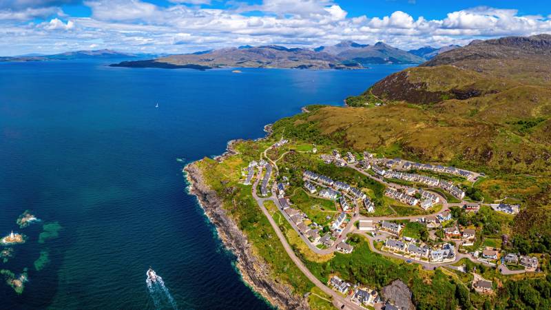 A picturesque coastal village nestles against a backdrop of rugged mountains and a vast, tranquil blue sea.