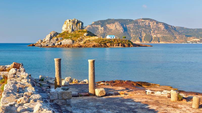 Ancient ruins and a charming blue-domed church dot a rocky island in the azure Aegean Sea.