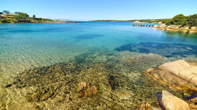 Crystal-clear turquoise waters lap gently against a rocky shore under a brilliant blue sky.