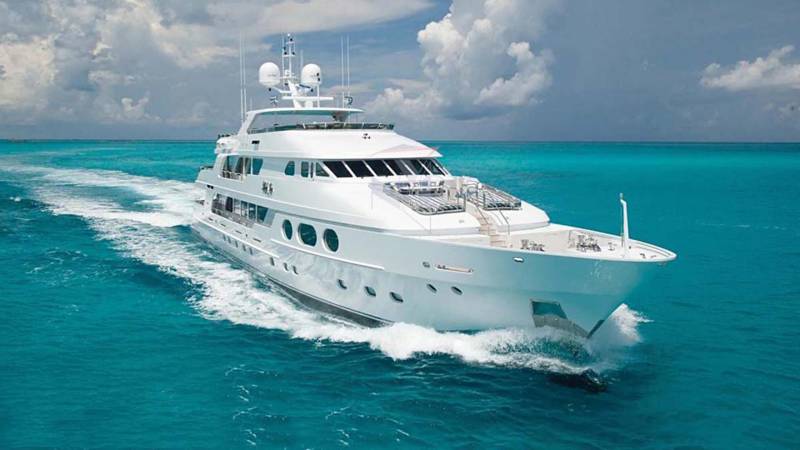 A sleek white yacht cruises through vibrant turquoise waters under a dramatic cloudy sky.