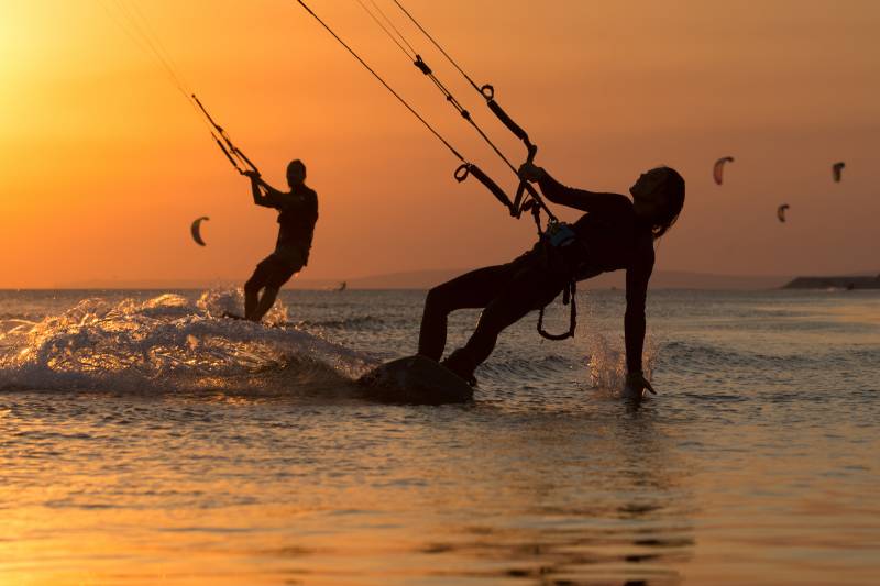 Silhouetted kitesurfers carve through the golden ocean waters at sunset.