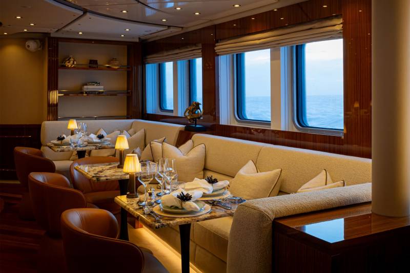A cozy and elegant dining area with large windows offering a scenic view, featuring plush seating, a table set with dinnerware, and a warm, inviting atmosphere.