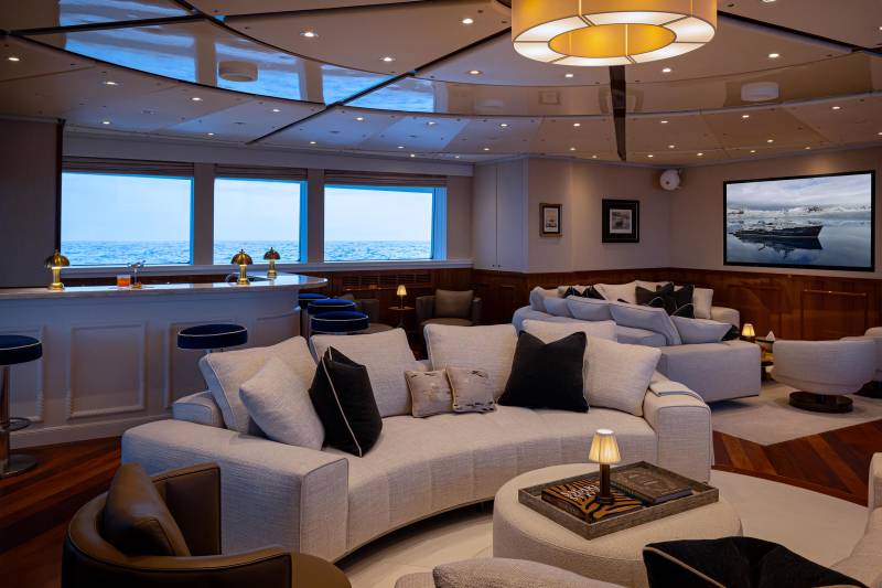 A cozy and luxurious living room with plush white sofas, a large circular window overlooking a scenic ocean view, and a warm lighting fixture creating a serene and inviting atmosphere.