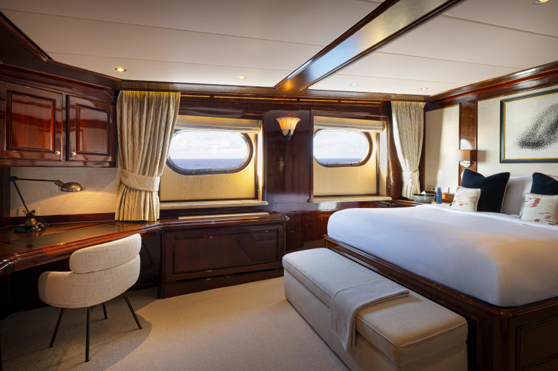 A cozy and luxurious cabin interior with wooden furnishings, large windows offering scenic views, and a comfortable-looking bed and seating area.